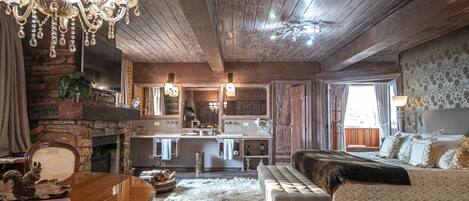 A rustic interior with a chandelier, wooden ceiling, a fireplace, a sofa, and a dining table.