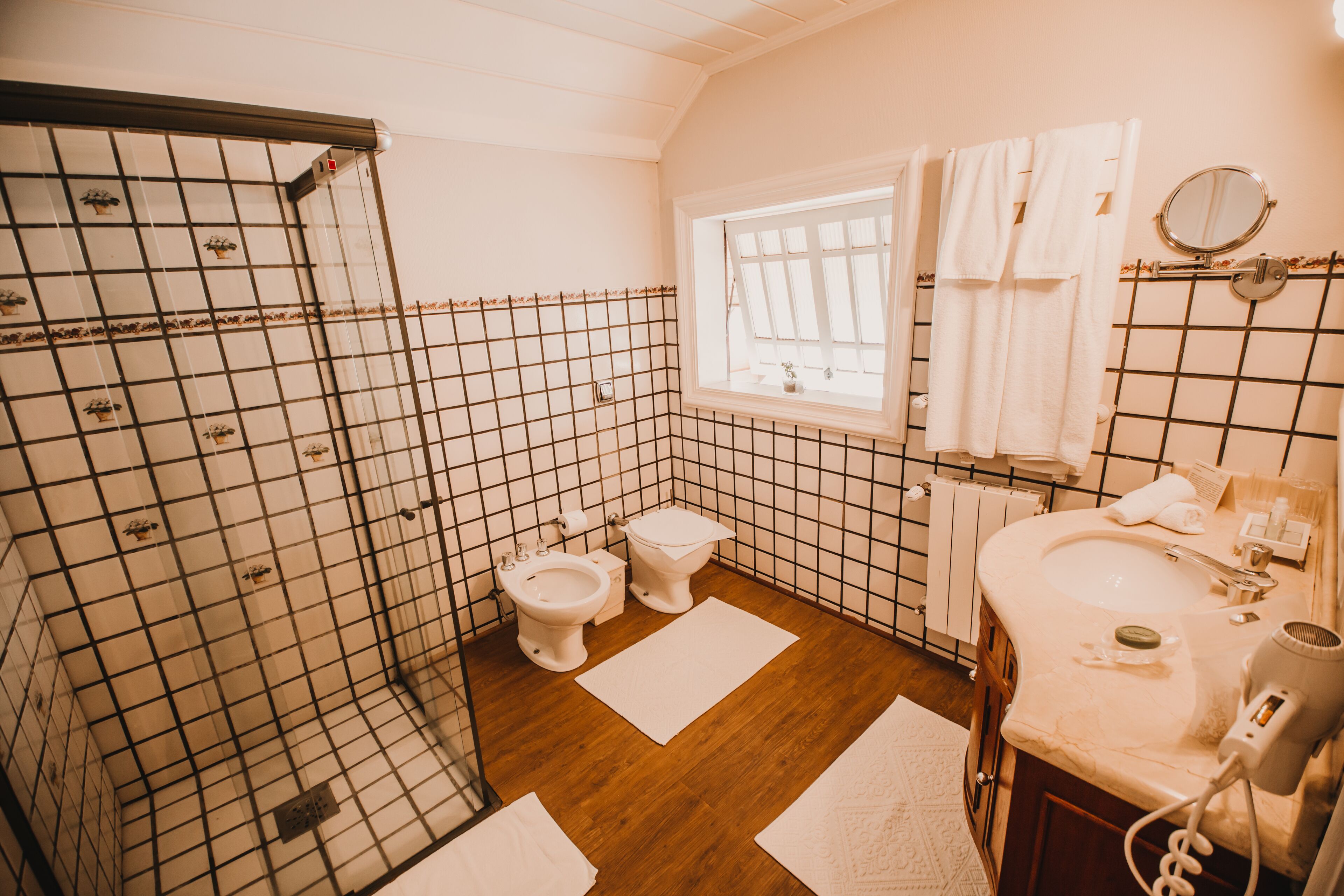 Een badkamer met een douche, twee toiletten, een wastafel en een raam.