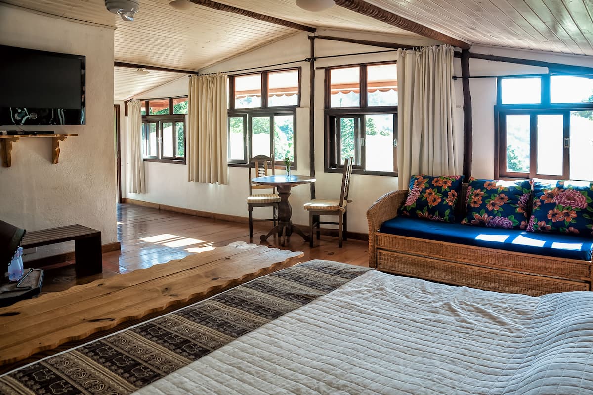 A cozy room with a bed, a wicker sofa with floral cushions, a small table, and a TV mounted on the wall.