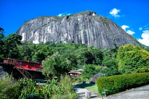 A large rock formation with a red building and a bridge in the foreground. - Pousada Paraíso Açú (Petrópolis)