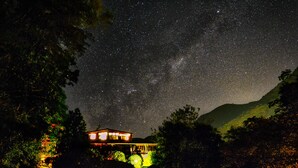 Una casa bajo un cielo estrellado, rodeada de árboles y colinas.