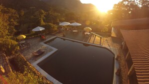 Zona de piscina con mobiliario exterior y sombrillas, rodeada de montañas y vegetación.
