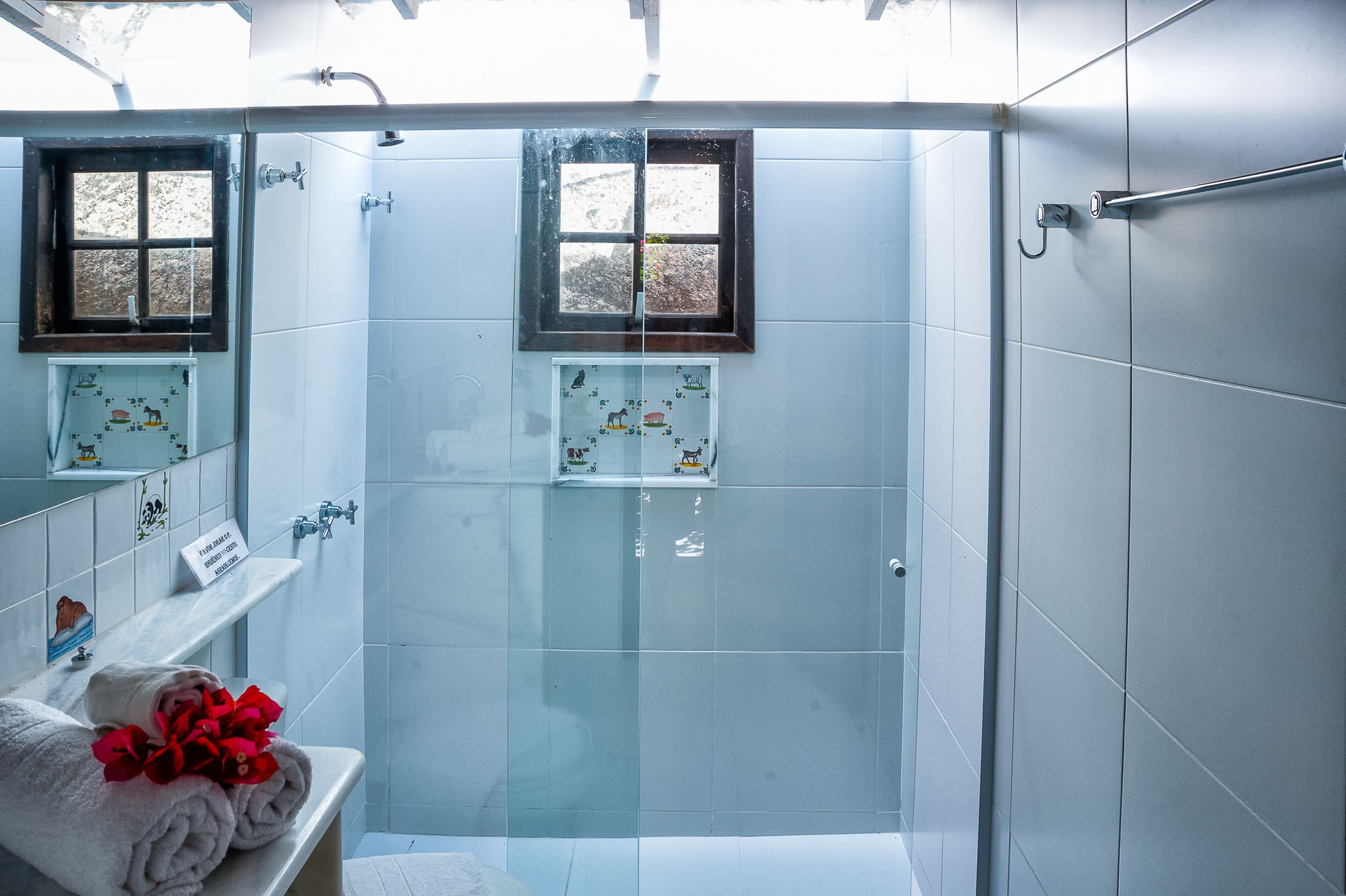 Une salle de bain moderne avec une douche à parois de verre, deux fenêtres et un porte-serviettes avec des serviettes.