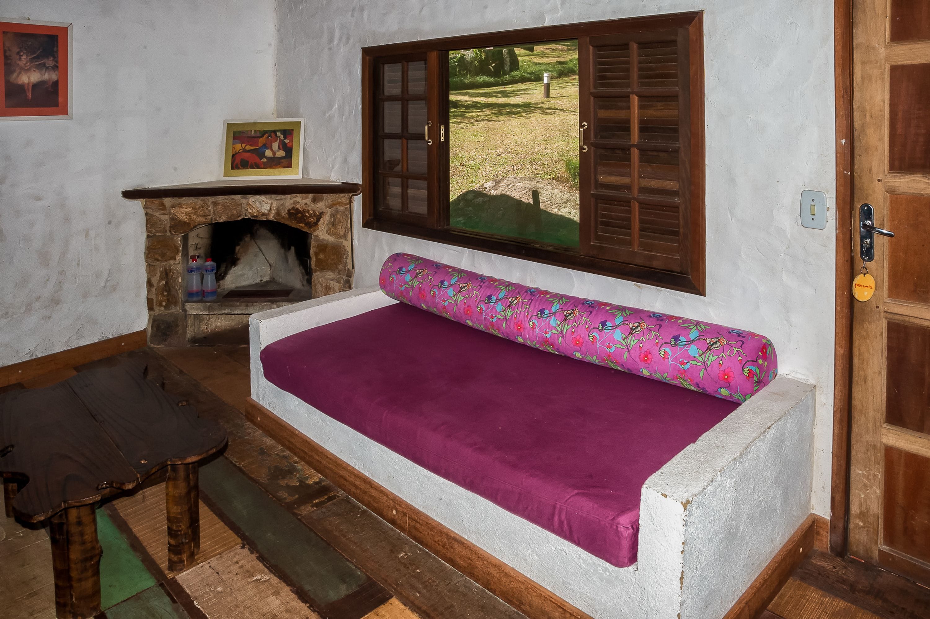 Ein gemütlicher Raum mit Kamin aus Stein, einer Bank, einem Sofa mit violettem Kissen und einer Holztür.