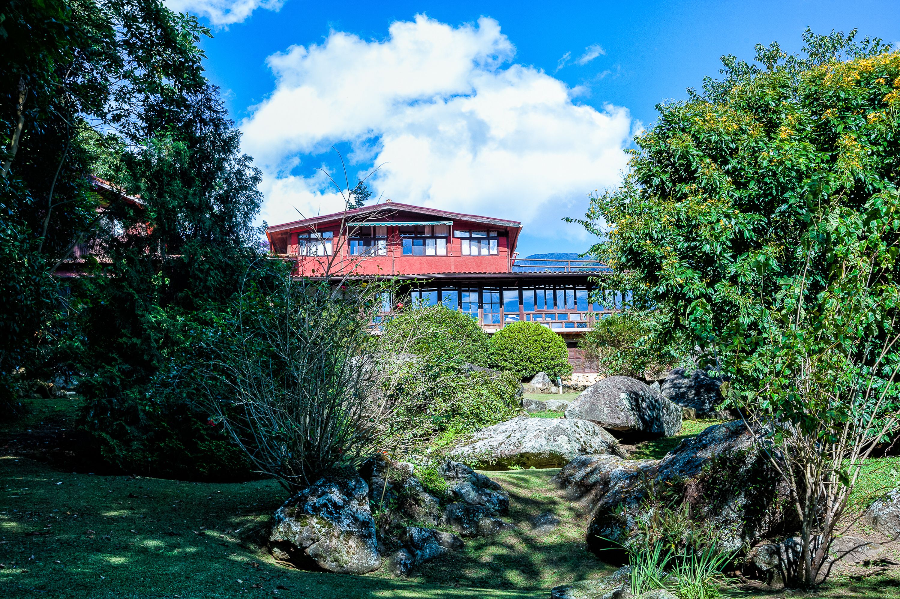 A red building with a flat roof, surrounded by large rocks and greenery.