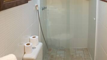 A small bathroom with a toilet, a glass-enclosed shower, and a window with blinds.