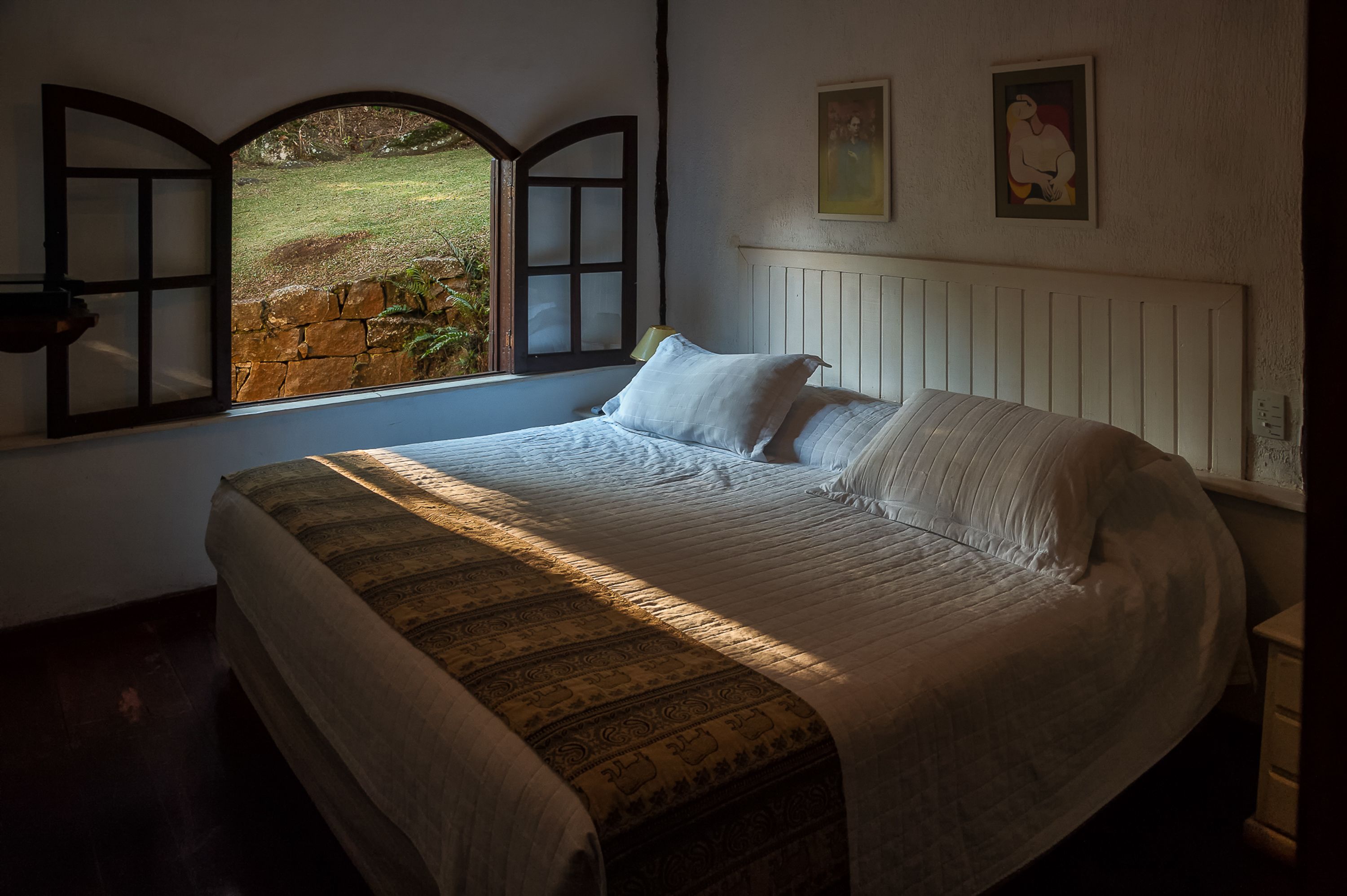 Une chambre avec un grand lit, une fenêtre donnant sur un jardin et un tableau accroché au mur.