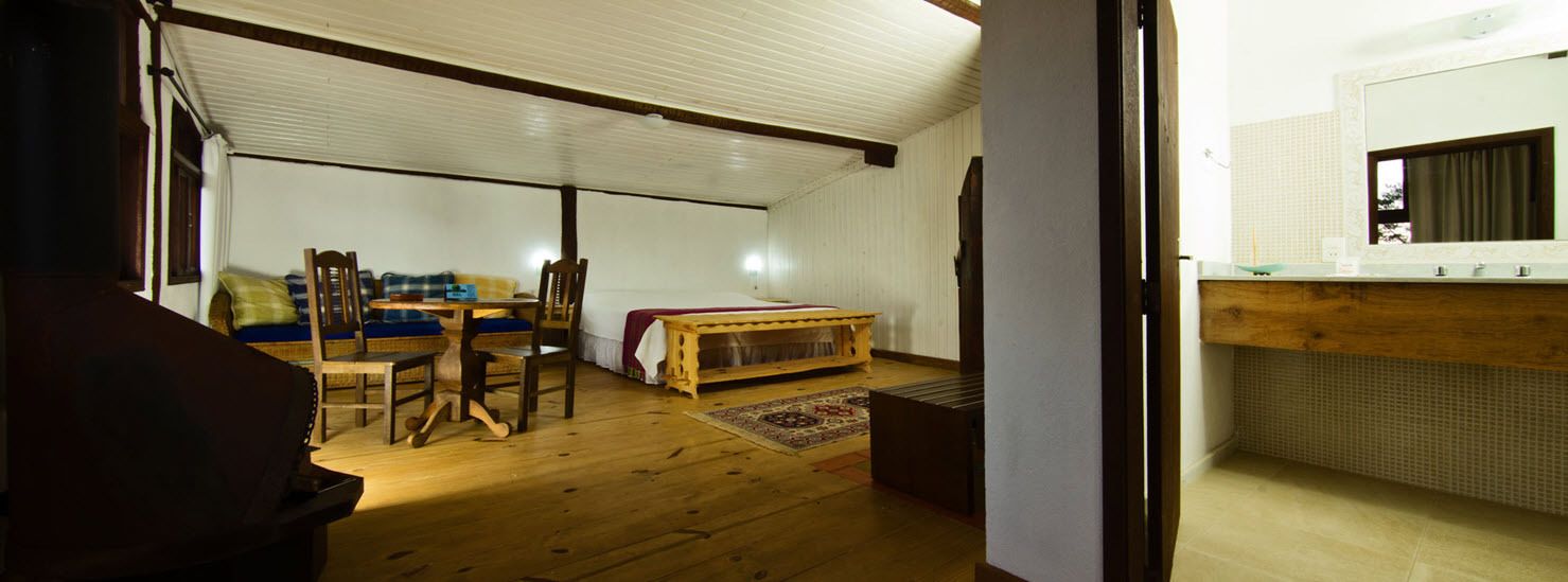 A room with a wooden floor, a bed, a dining table with chairs, and a small wooden bench.