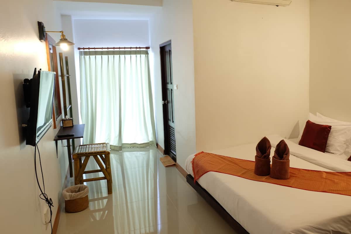 A hotel room with a bed, a desk with a lamp, a chair, and a window with curtains.