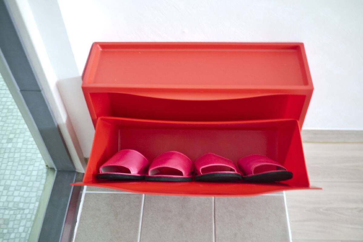 A red storage box with multiple compartments, likely for shoes, placed on a tiled floor near a white wall.