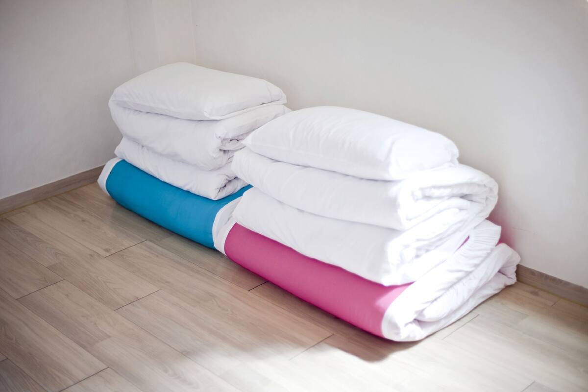 A stack of neatly folded white and pink bedding in a corner of a room with wooden flooring.