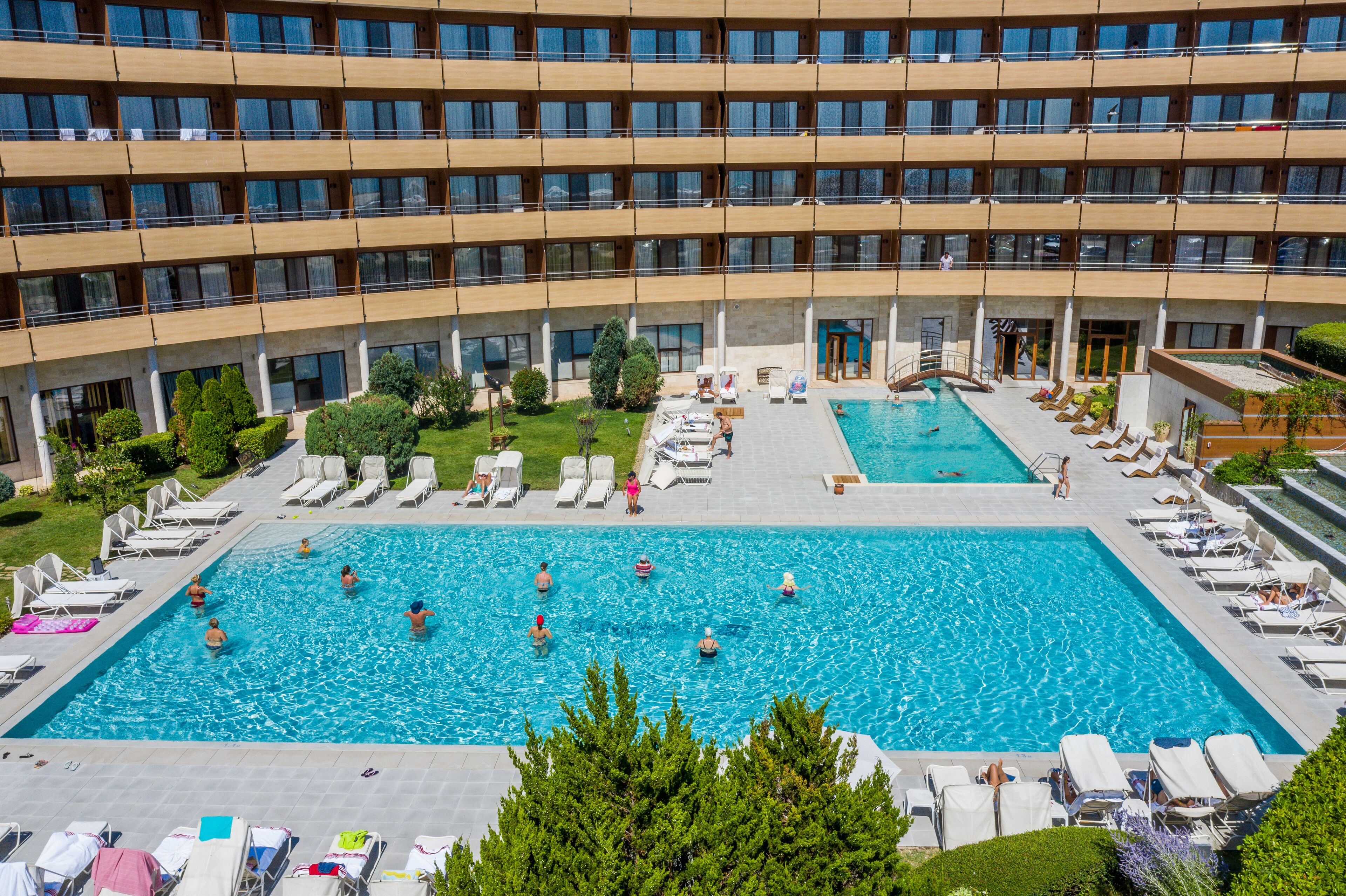 Een meerlaags hotel met een centraal gelegen zwembad, omringd door ligbedden en een kleiner zwembad.