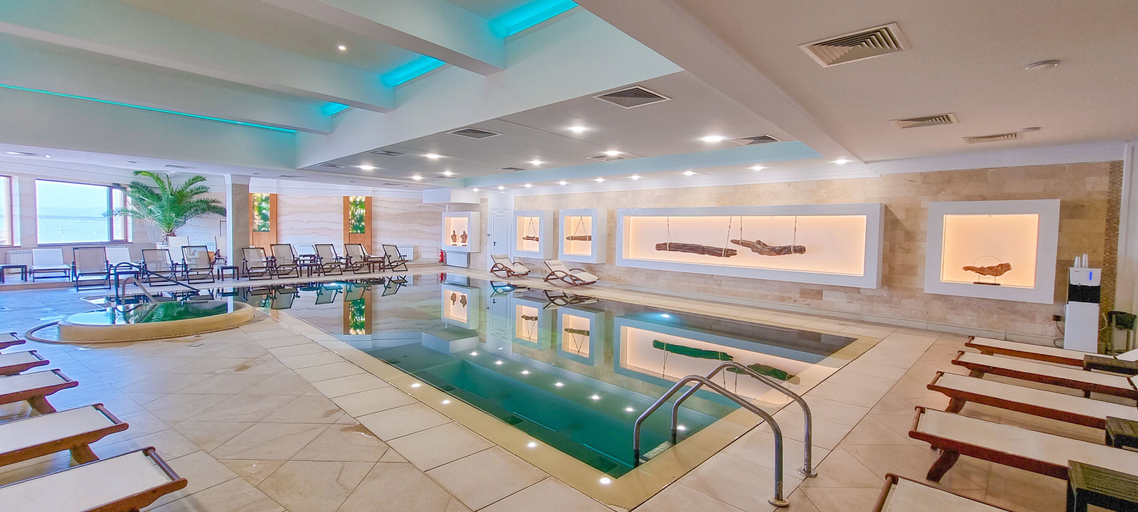 A hotel lobby with a large indoor pool, seating areas, and wall-mounted displays.