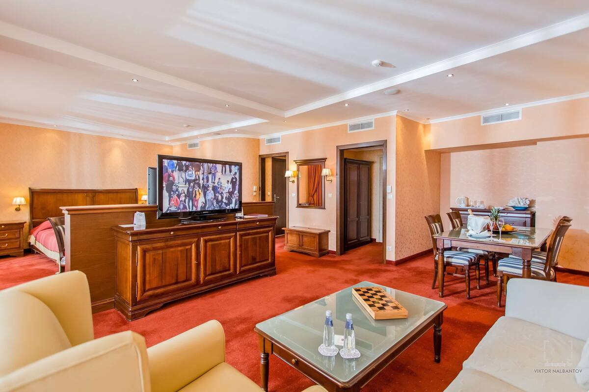 Una habitación de hotel con televisión, un escritorio de madera, una mesa de comedor y un tablero de ajedrez.