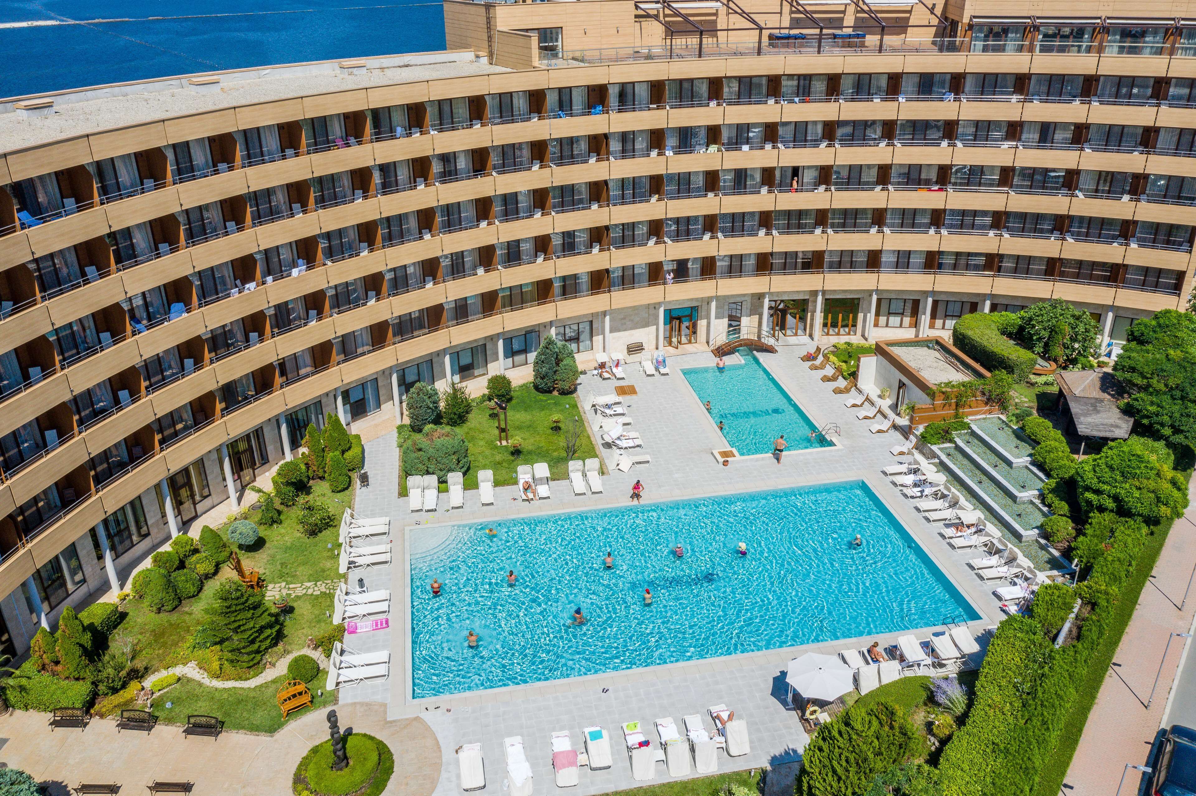 A hotel with multiple floors, a central swimming pool, and surrounding greenery.