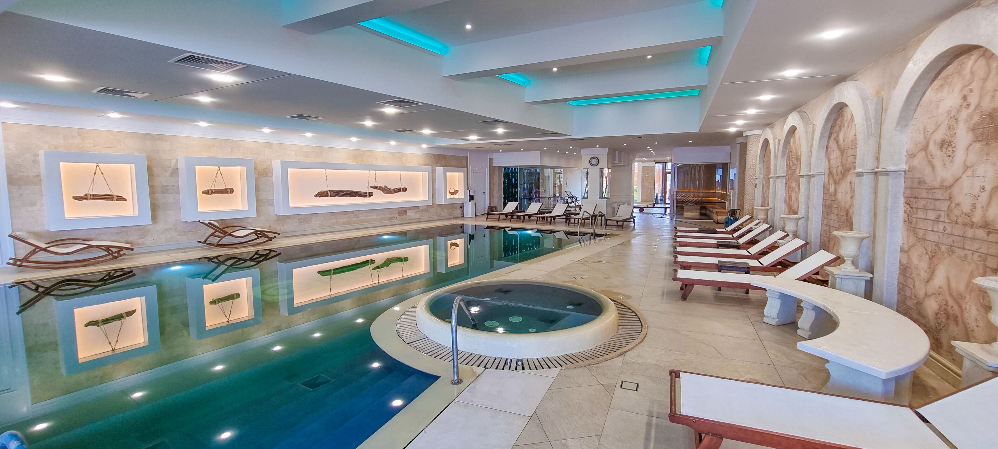 A modern indoor pool area with lounge chairs, a hot tub, and wall-mounted artwork.