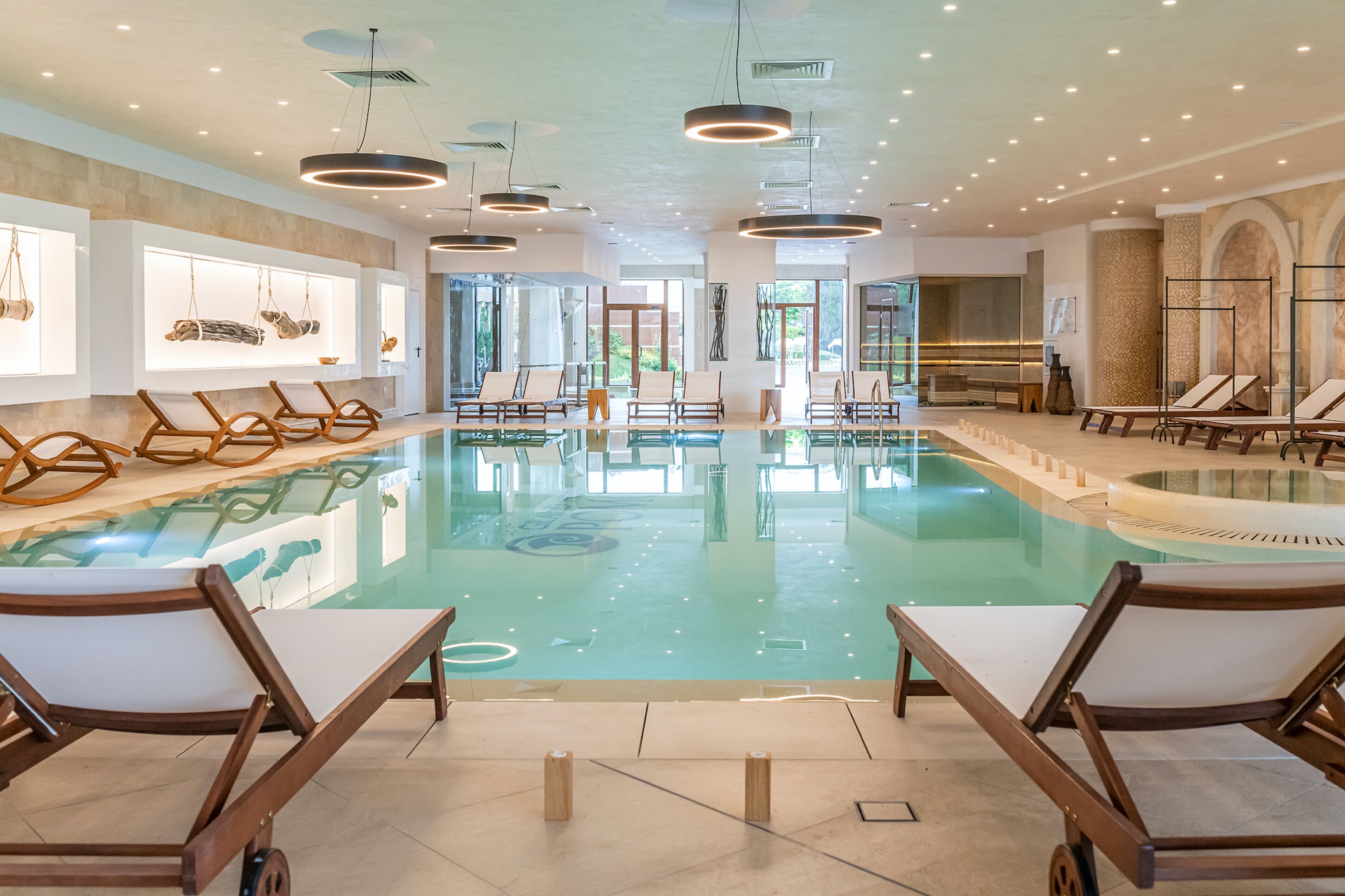 Una piscina interior amplia con numerosas tumbonas e iluminación moderna.