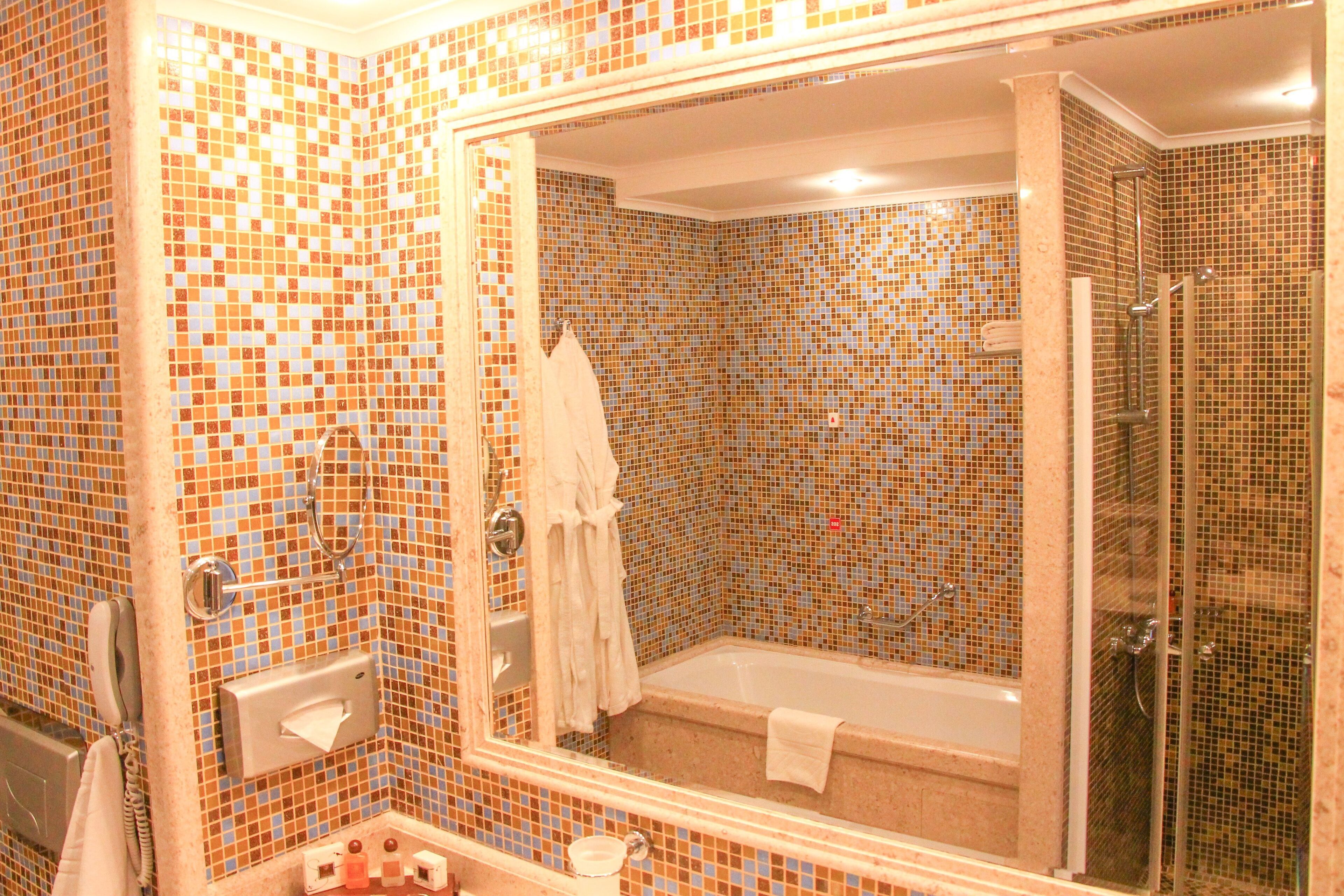 Un baño con paredes de mosaico, una bañera, una ducha y un espejo.