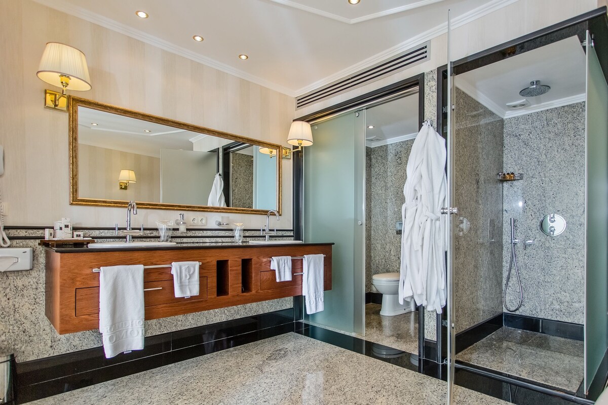 Un baño moderno con un espejo grande, un tocador con lavabo y una zona de ducha con paredes de vidrio.