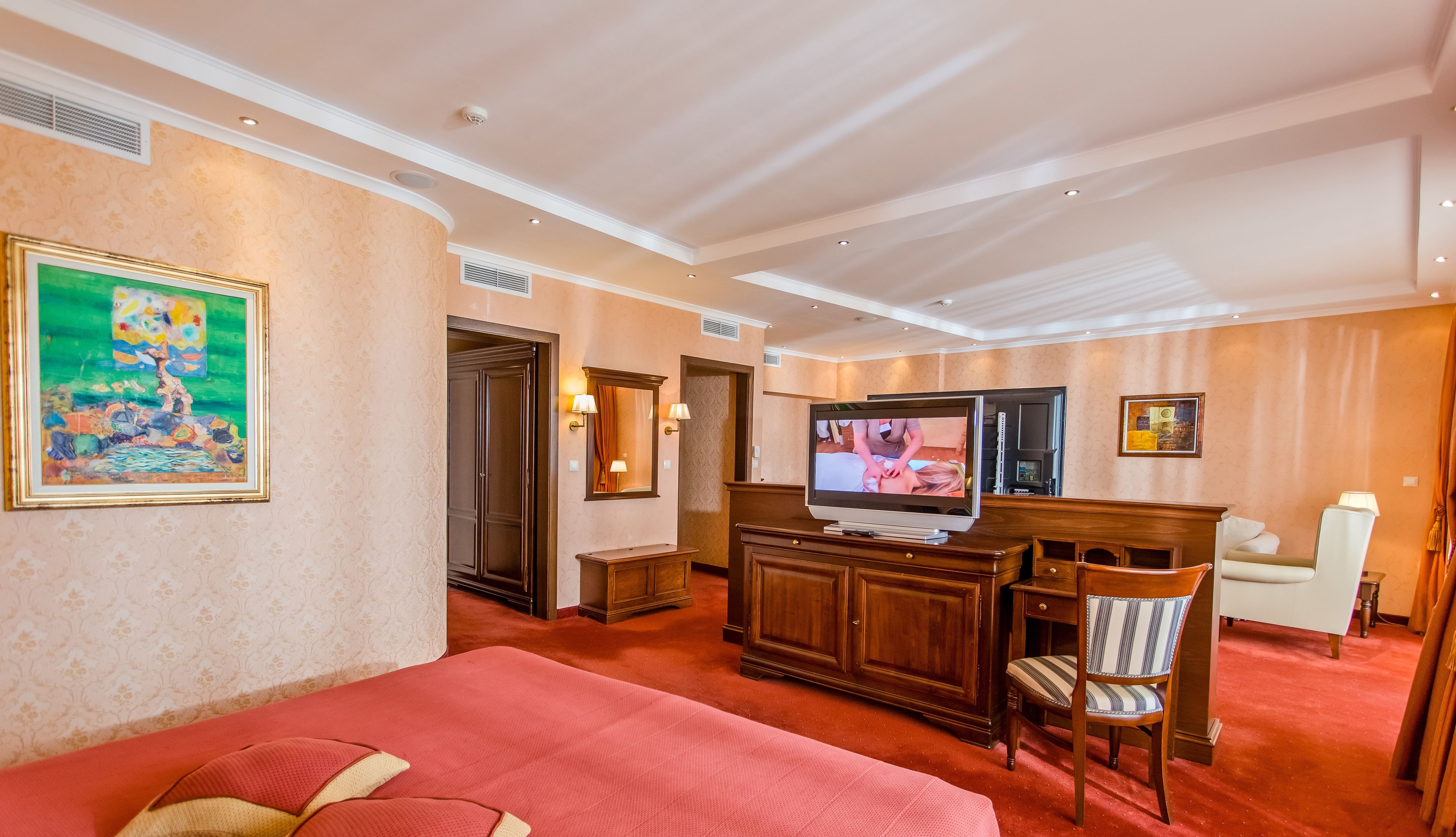 Habitación de hotel con una cama grande, televisión, mueble de madera, una silla y obras de arte en las paredes.