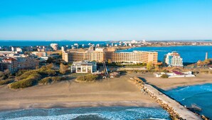Vista aérea de un complejo hotelero frente al mar, con varias construcciones, una playa y un muelle.