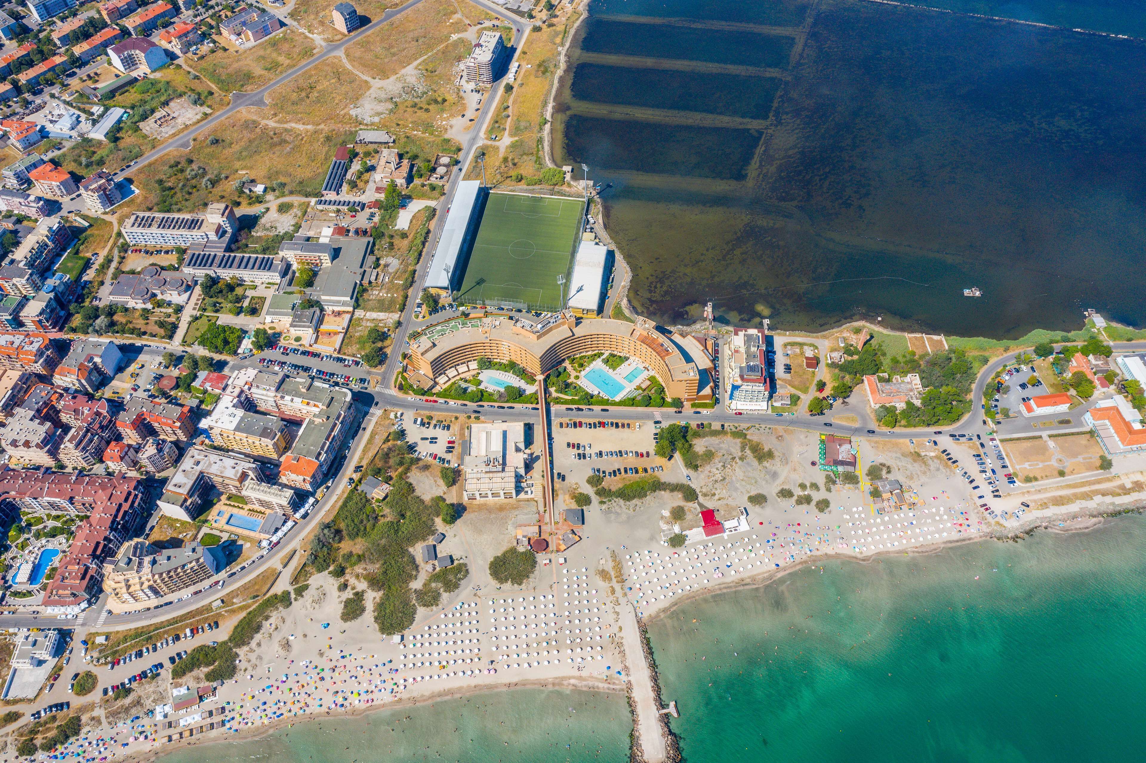 An aerial view of a coastal area with a stadium, beach, and surrounding buildings.