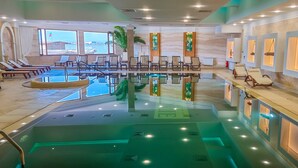 Una amplia piscina interior con agua cristalina, rodeada de sillas de descanso y una zona de recepción con detalles de madera.