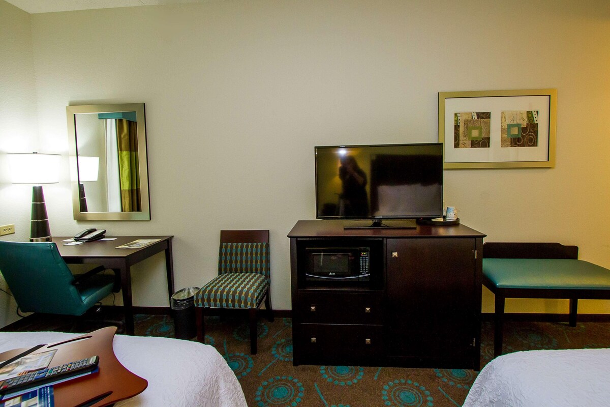 A hotel room with a bed, a desk, a chair, a television, a microwave, and a framed picture on the wall.