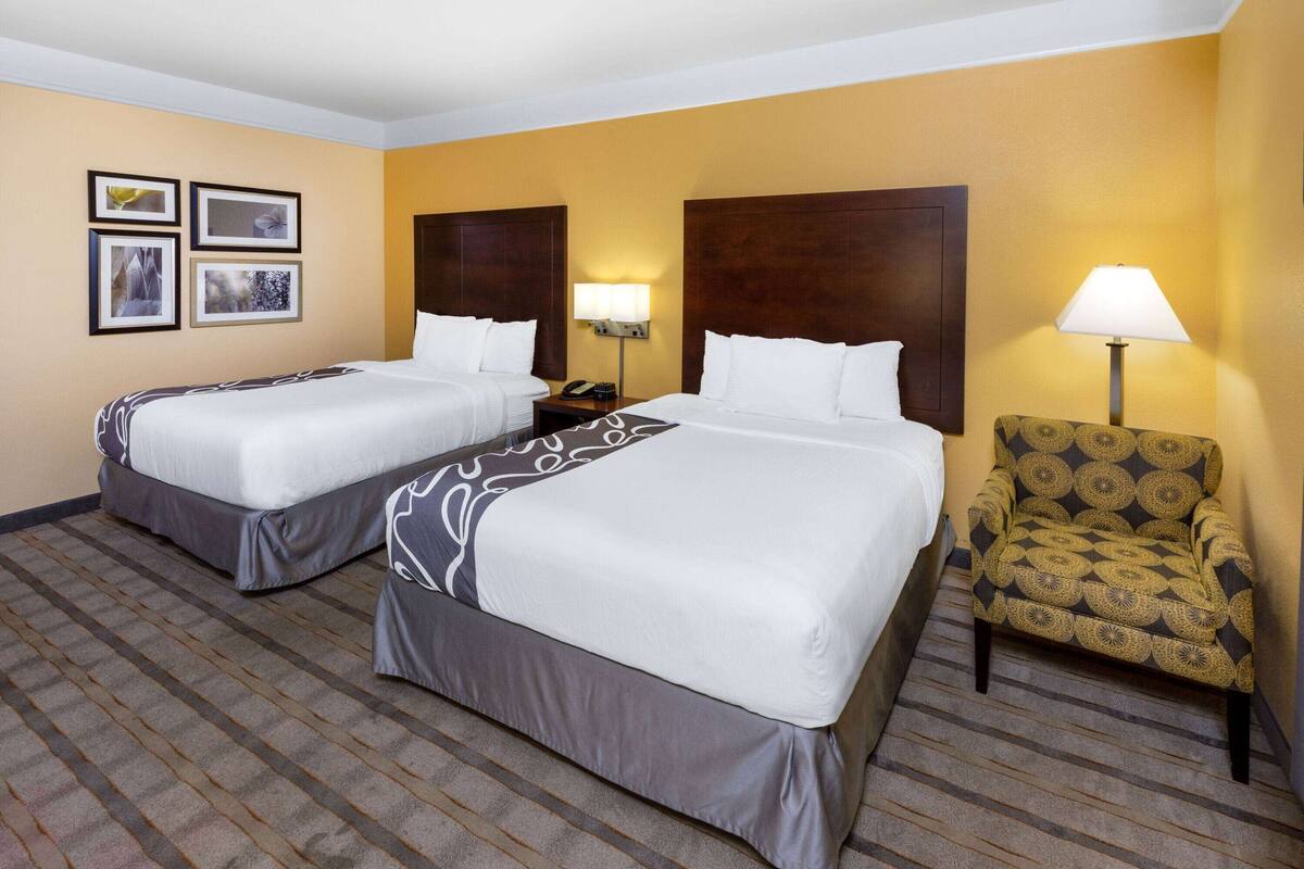 A hotel room with two beds, a chair, and a lamp.