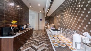 A modern hotel kitchen with a buffet setup, featuring a long counter with various food items and a patterned wall design.