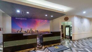A hotel reception area with two reception desks, a cityscape mural, a clock, and a patterned floor.