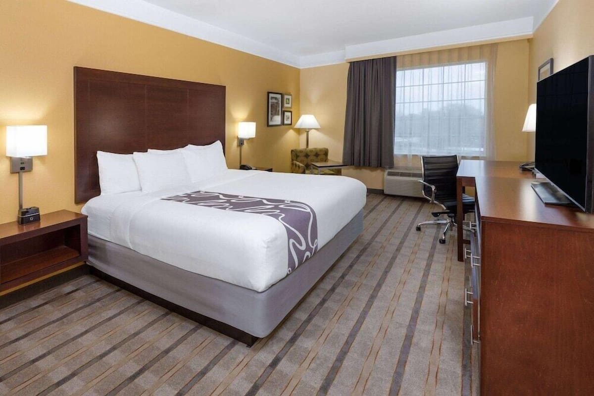 A hotel room with a large bed, a desk, a chair, a television, and a window with curtains.