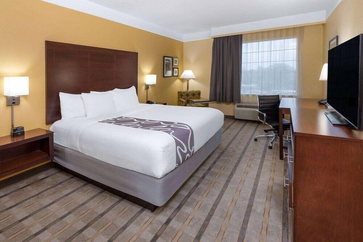 Una habitación de hotel con una cama grande, un escritorio, una silla, un televisor y una ventana con cortinas.
