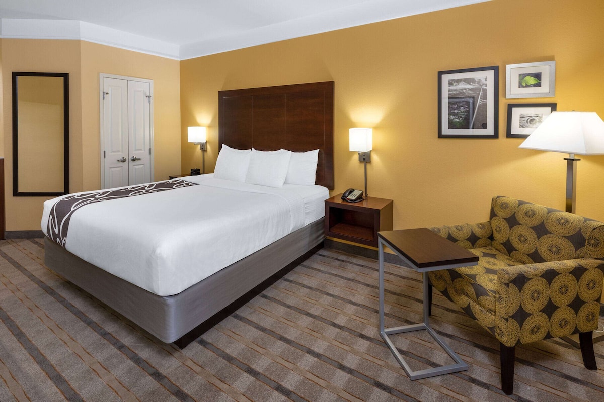 A hotel room with a large bed, a chair, a nightstand, and a lamp.