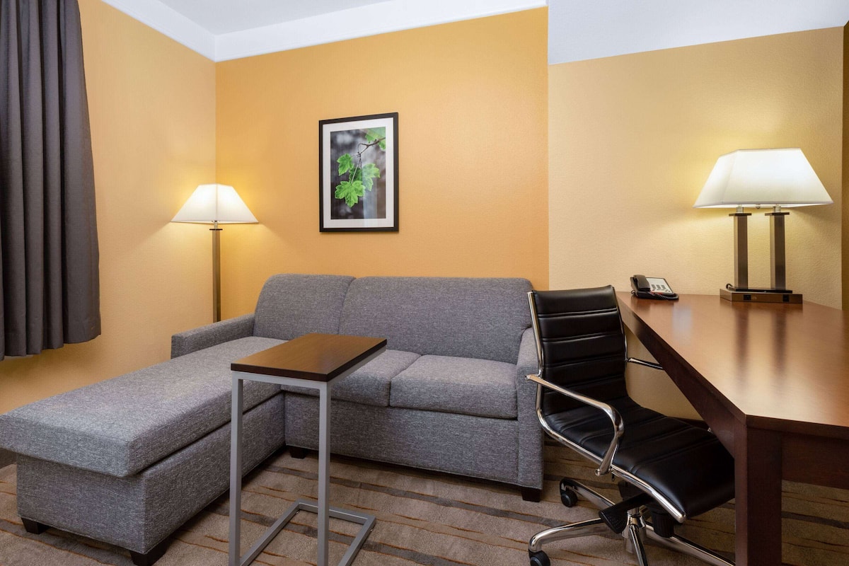 A hotel room with a grey sofa, a small table, a black office chair, and two lamps.