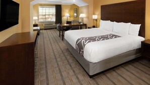 A hotel room with a large bed, a desk, a chair, a TV, and a window with curtains.