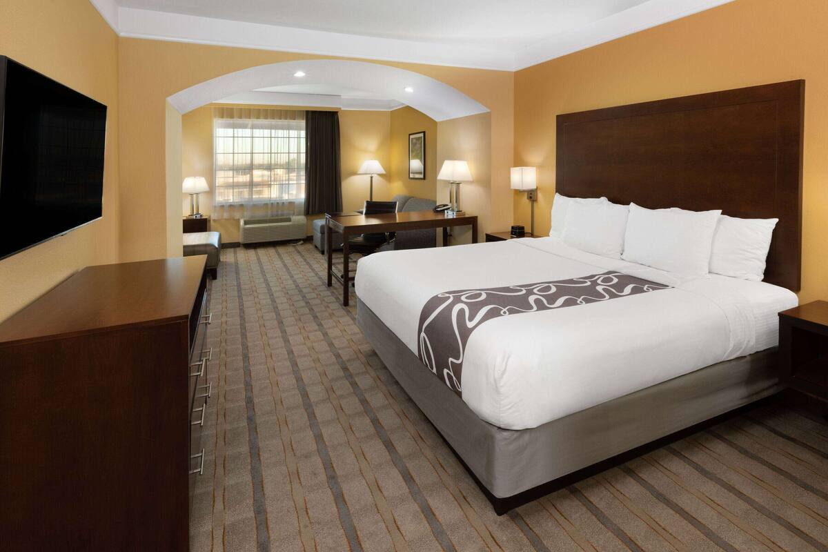 A hotel room with a large bed, a desk, a chair, a TV, and a window with curtains.