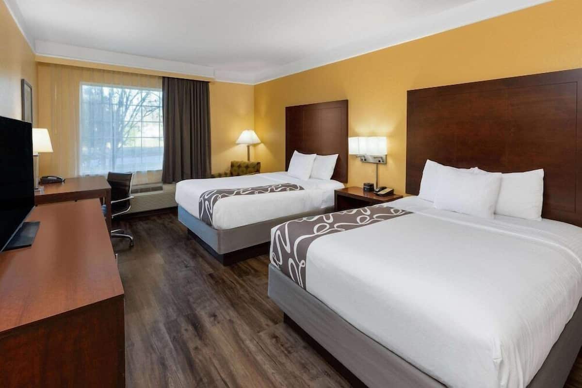 A hotel room with two beds, a desk, a chair, a TV, and a window with curtains.