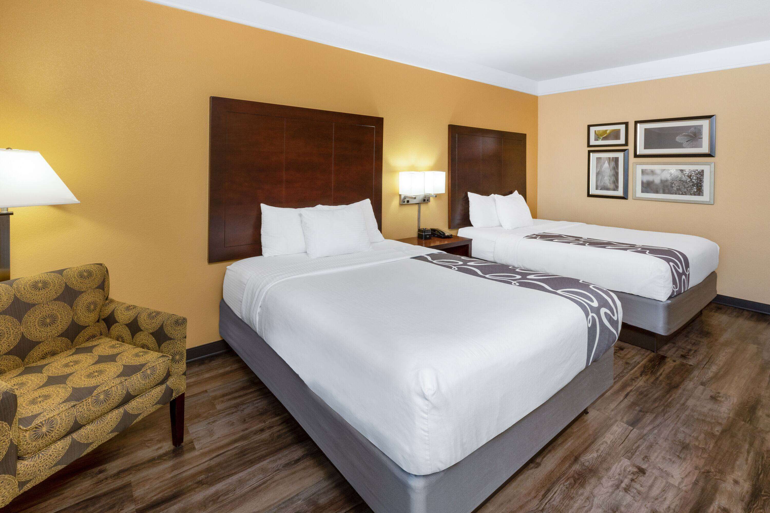 A hotel room with two beds, a sofa, a nightstand, and framed pictures on the wall.