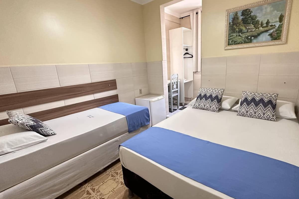 A bedroom with two beds, a small desk, a chair, and a painting on the wall.