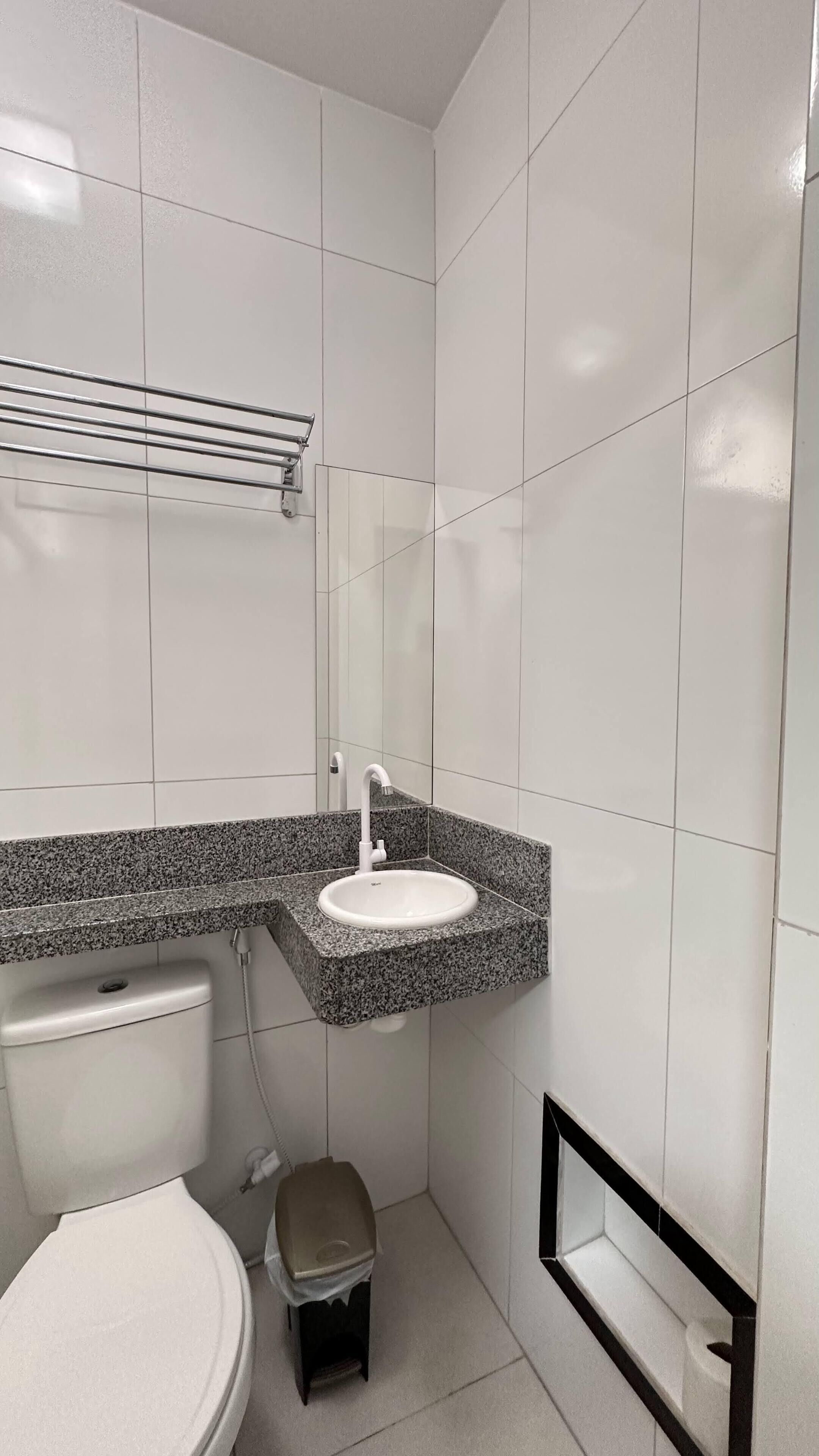 A small, modern bathroom with white tiles, a granite countertop sink, a toilet, and a small stool.