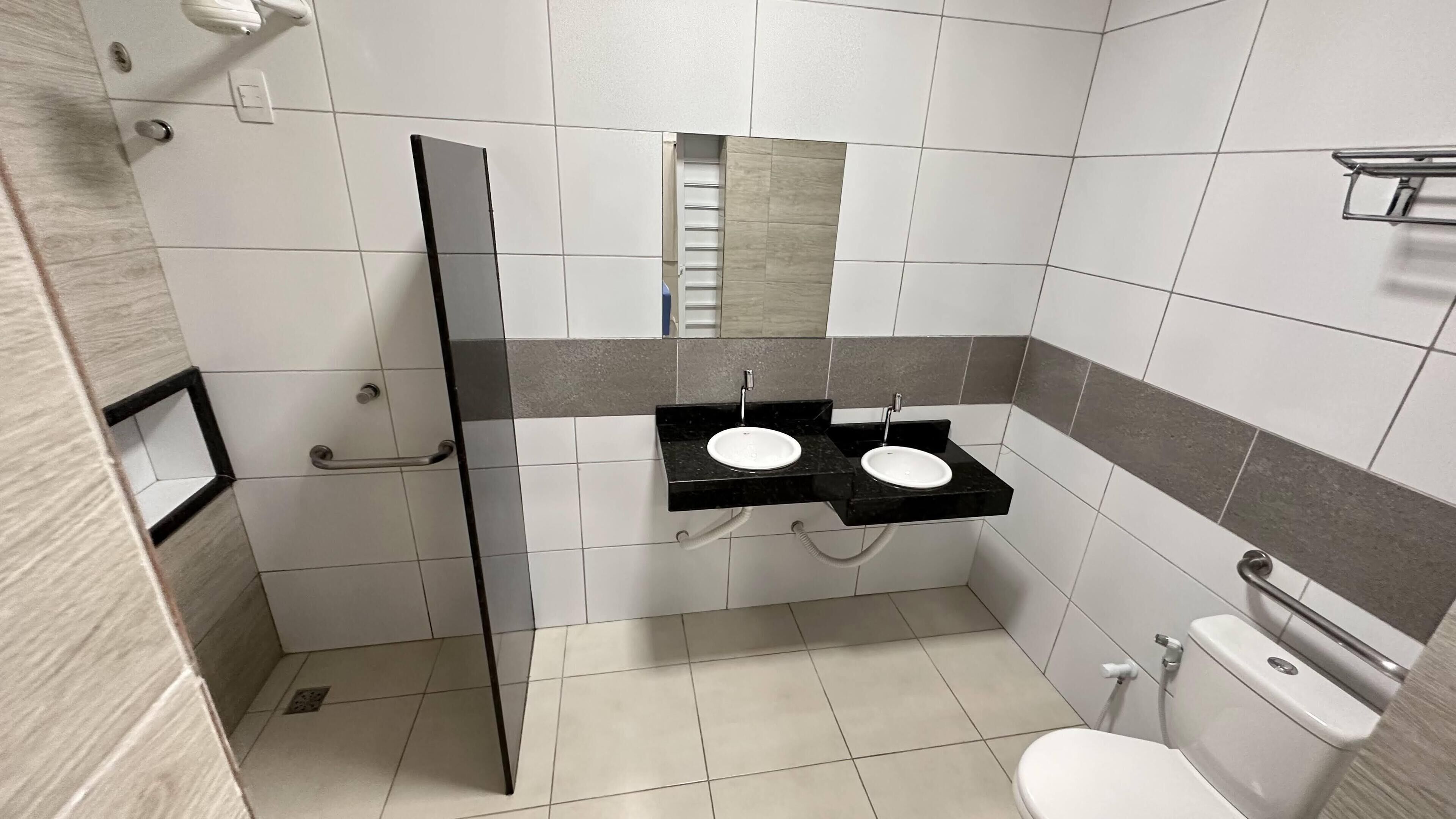Et moderne badeværelse med en glasbrusekabine, to håndvaske og et toilet.