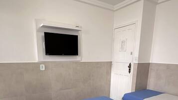 A hotel room with two beds, a flat-screen TV mounted on the wall, a door with a lock, and a tiled floor.