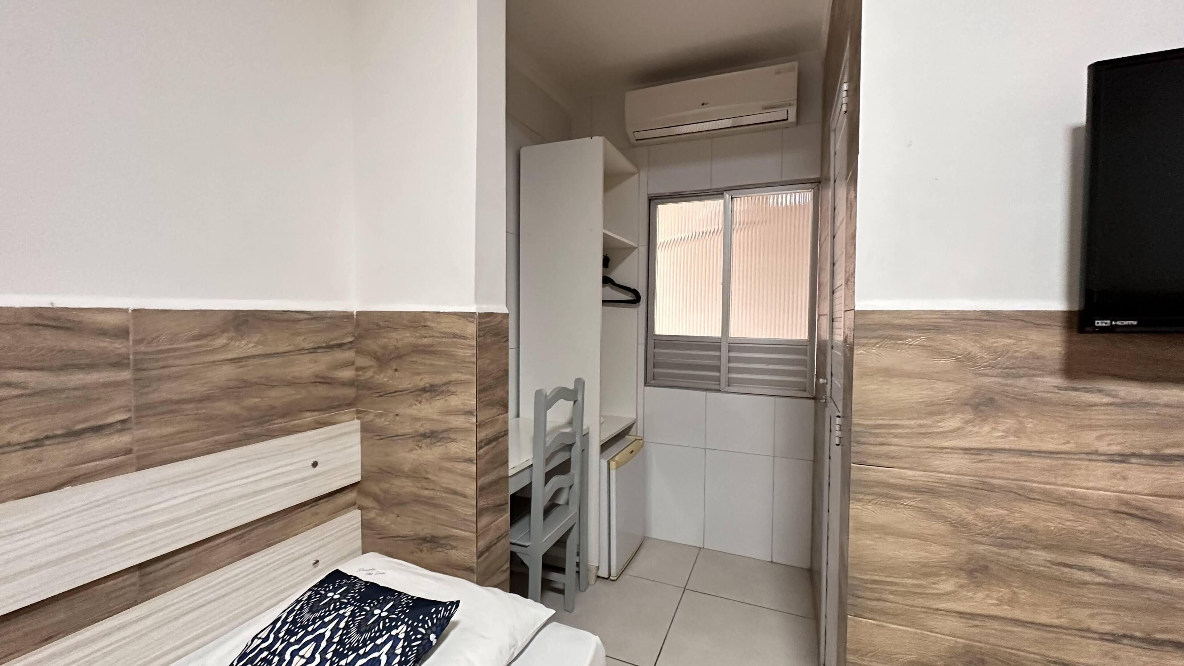A compact room with a bed, a small desk with a chair, a wardrobe, and a television.