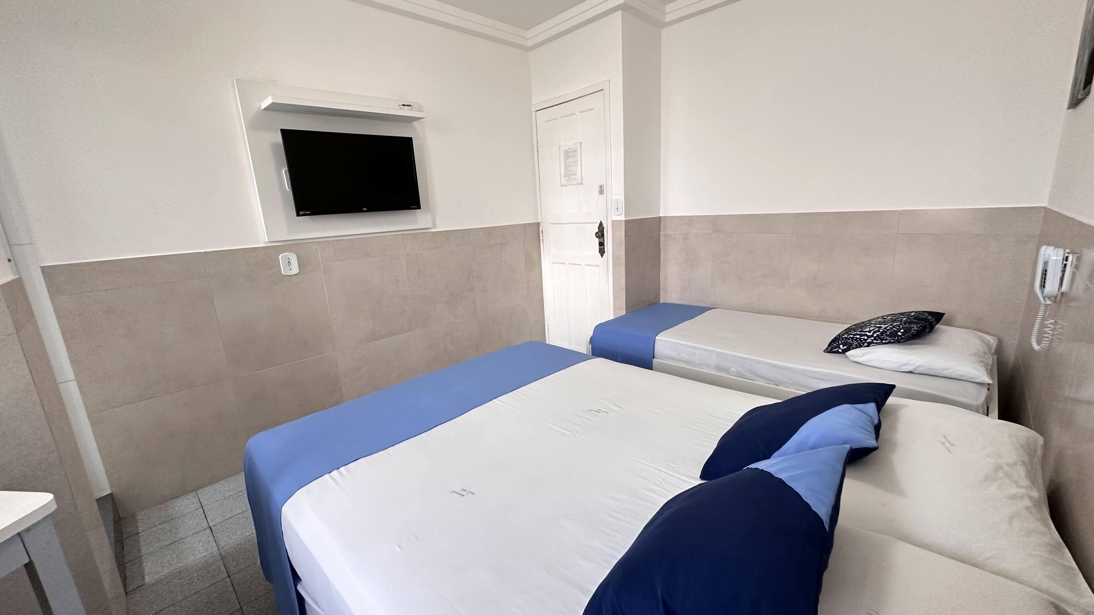 Habitación de hotel con dos camas, un televisor fijado a la pared, una puerta y un teléfono en la pared.