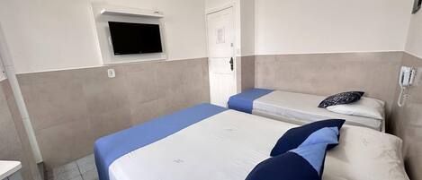 Habitación de hotel con dos camas, un televisor fijado a la pared, una puerta y un teléfono en la pared.
