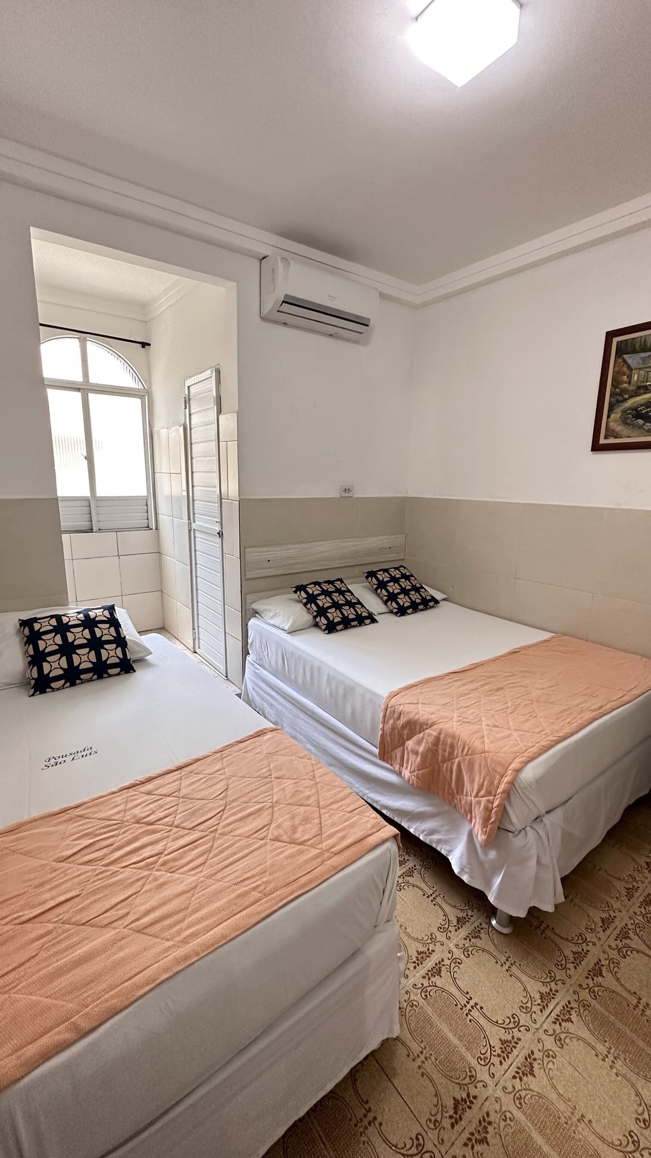 Une chambre d’hôtel avec deux lits simples, une fenêtre donnant sur un beau paysage, un appareil de climatisation et un tableau au mur.
