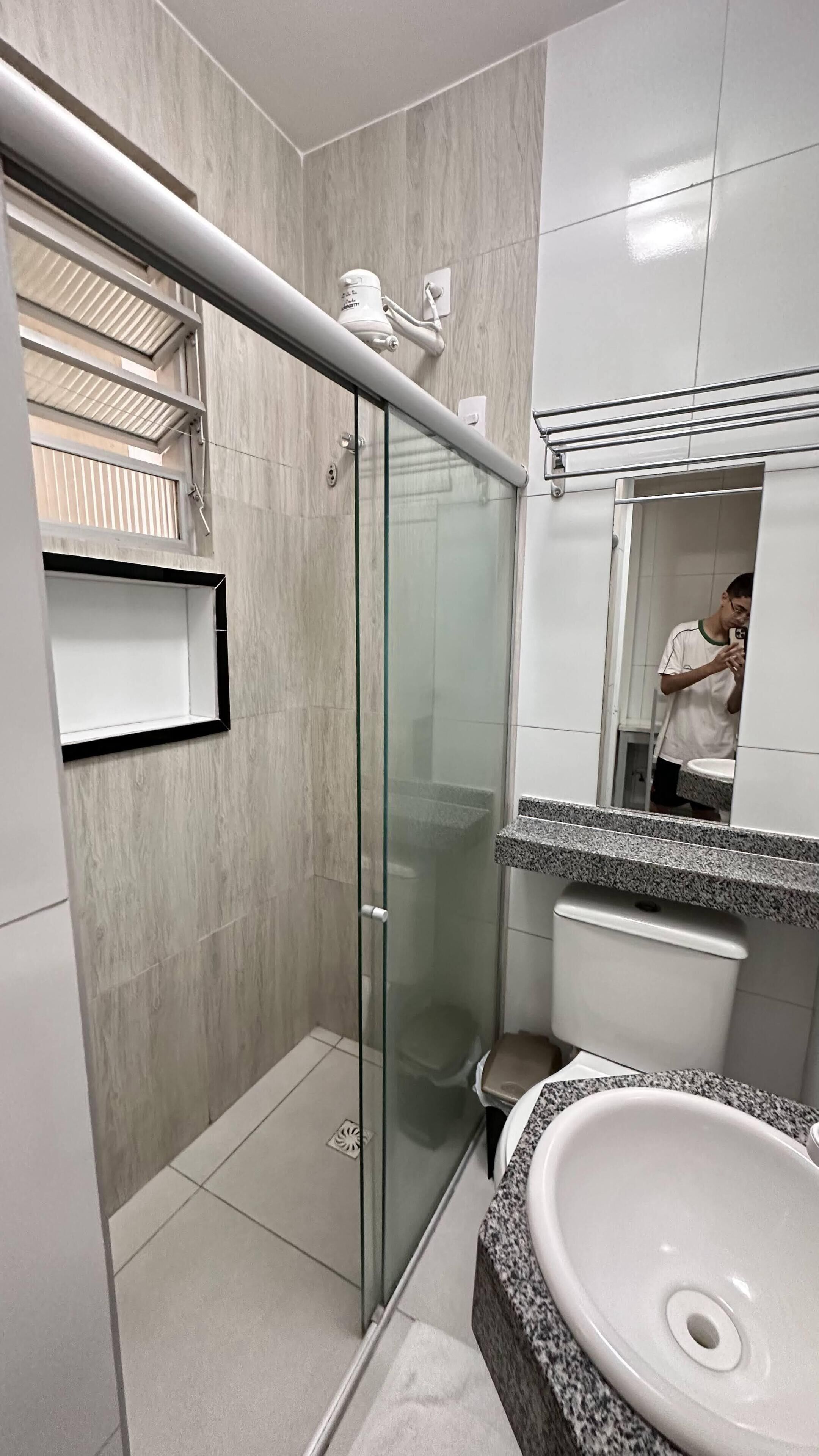 A modern bathroom with a glass shower enclosure, a white sink with a granite countertop, and a mirror reflecting a person.