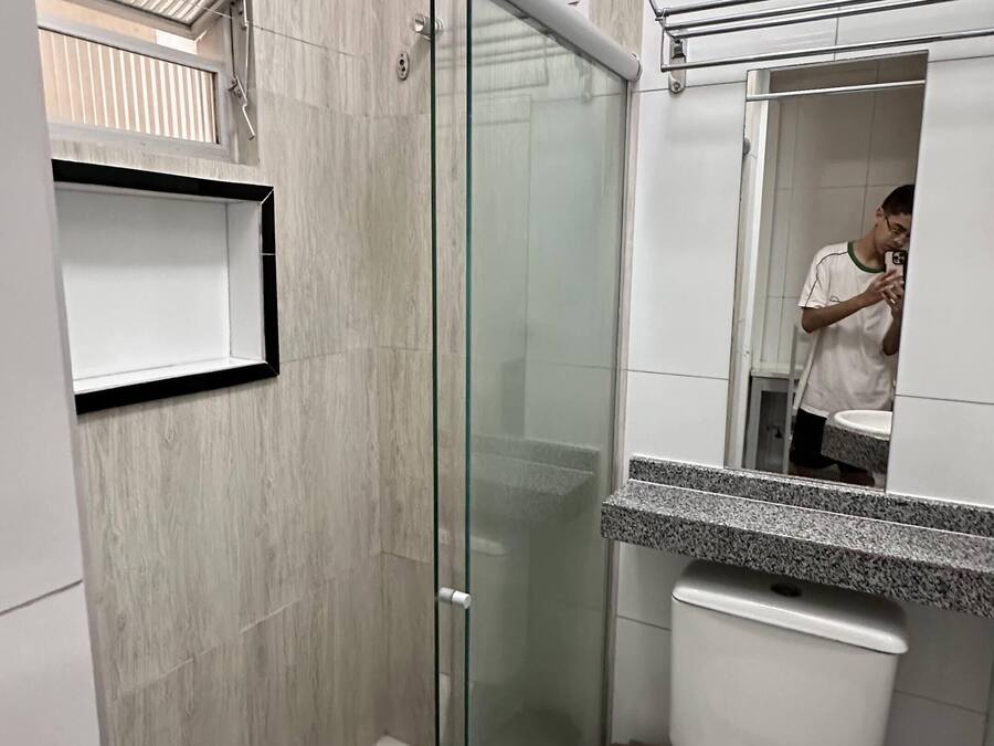 A modern bathroom with a glass shower enclosure, a white sink with a granite countertop, and a mirror reflecting a person.