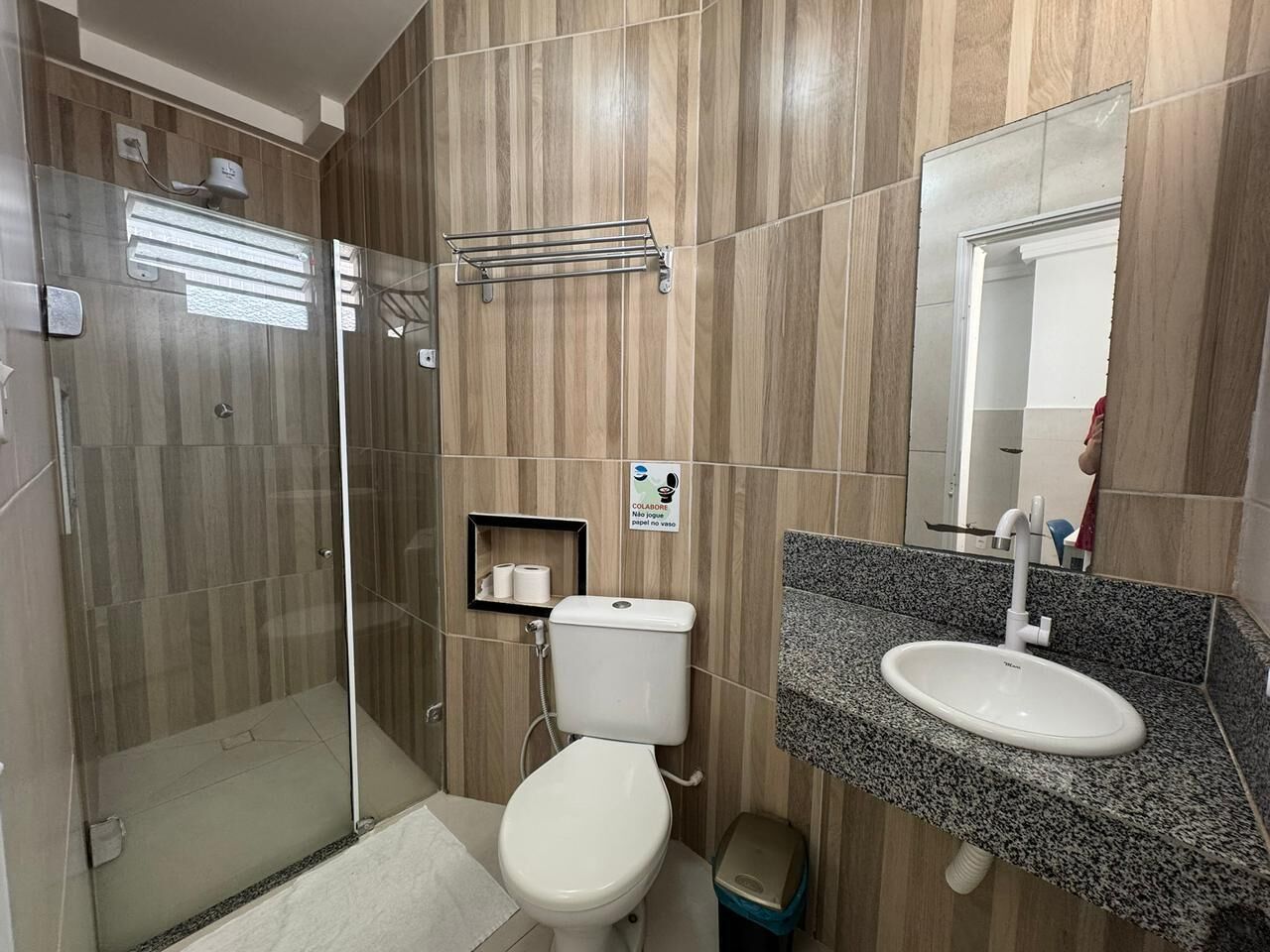 Casa de banho com cabine de chuveiro em vidro, sanita, lavatório com bancada de granito e espelho.